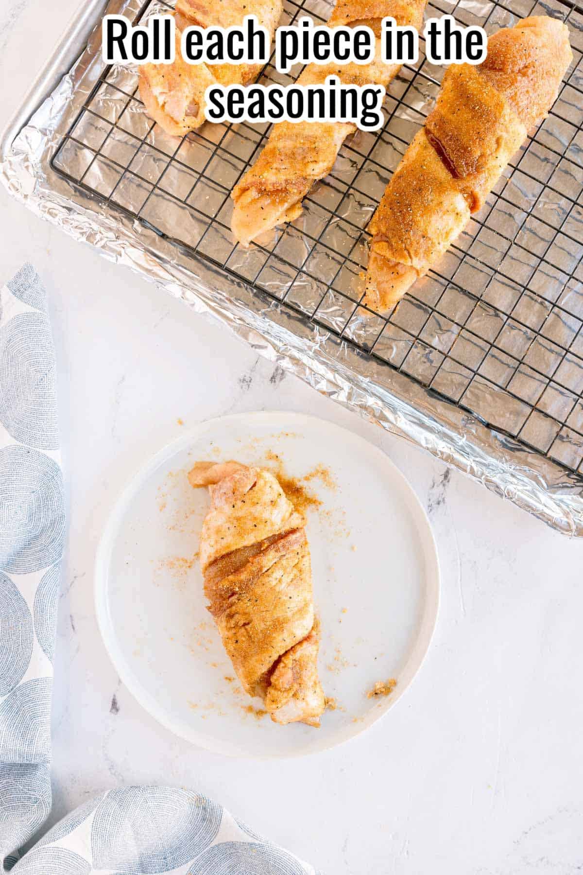 Bacon wrapped chicken rolled in seasoning on a rack. Text on the image says 'Roll each piece in the seasoning'.