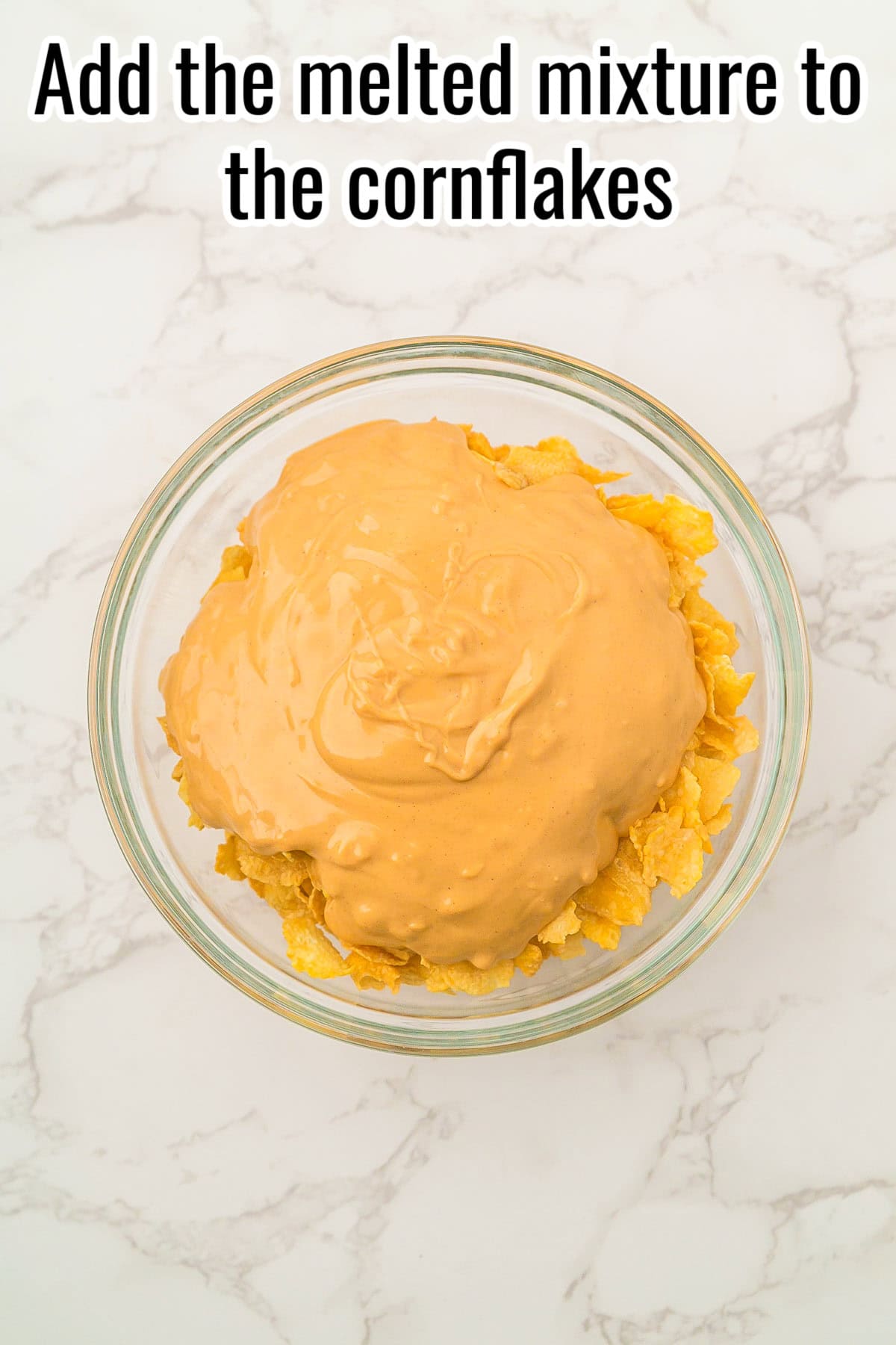 Melted mixture poured over cornflakes in a glass bowl. Text on the image says 'Add the melted mixture to the cornflakes'.