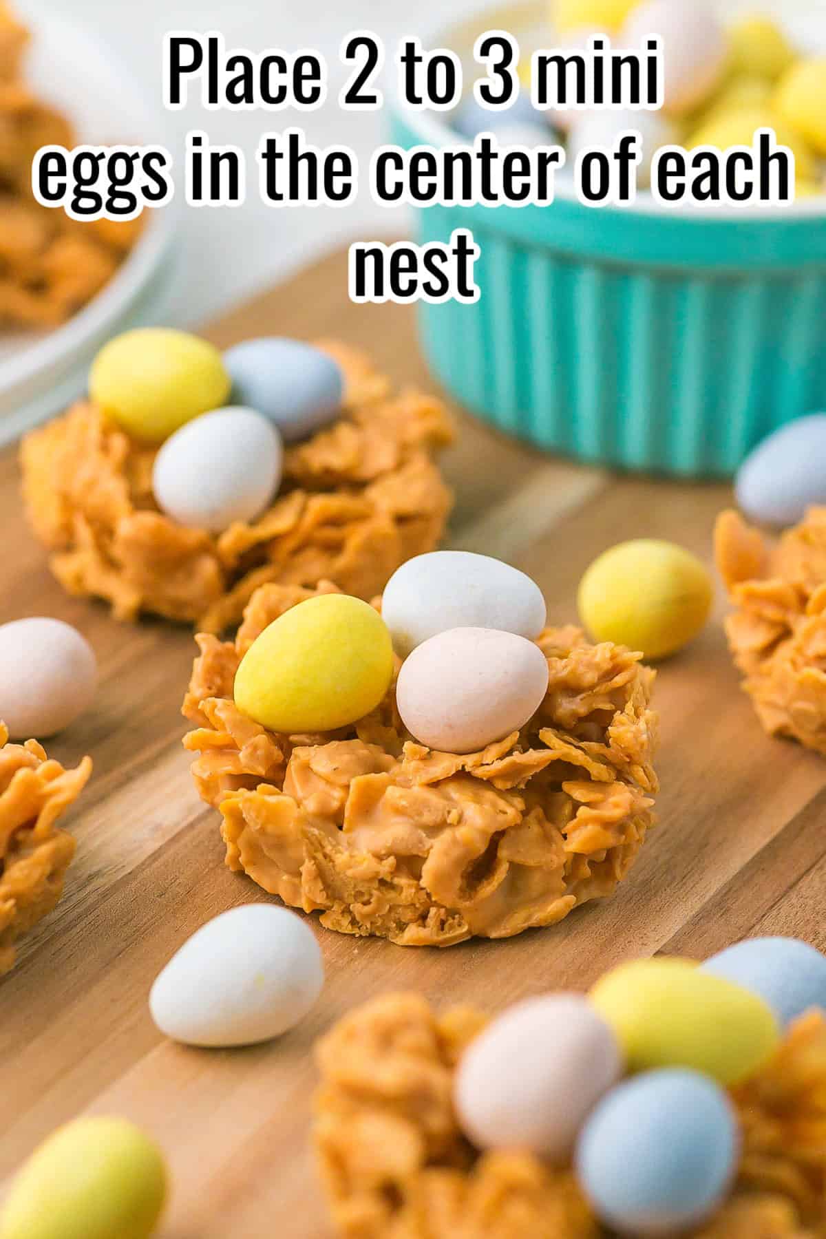 Bird’s nest cookies topped with pastel candy eggs on a wooden board. Text on the image says 'Place 2 to 3 mini eggs in the center of each nest'.