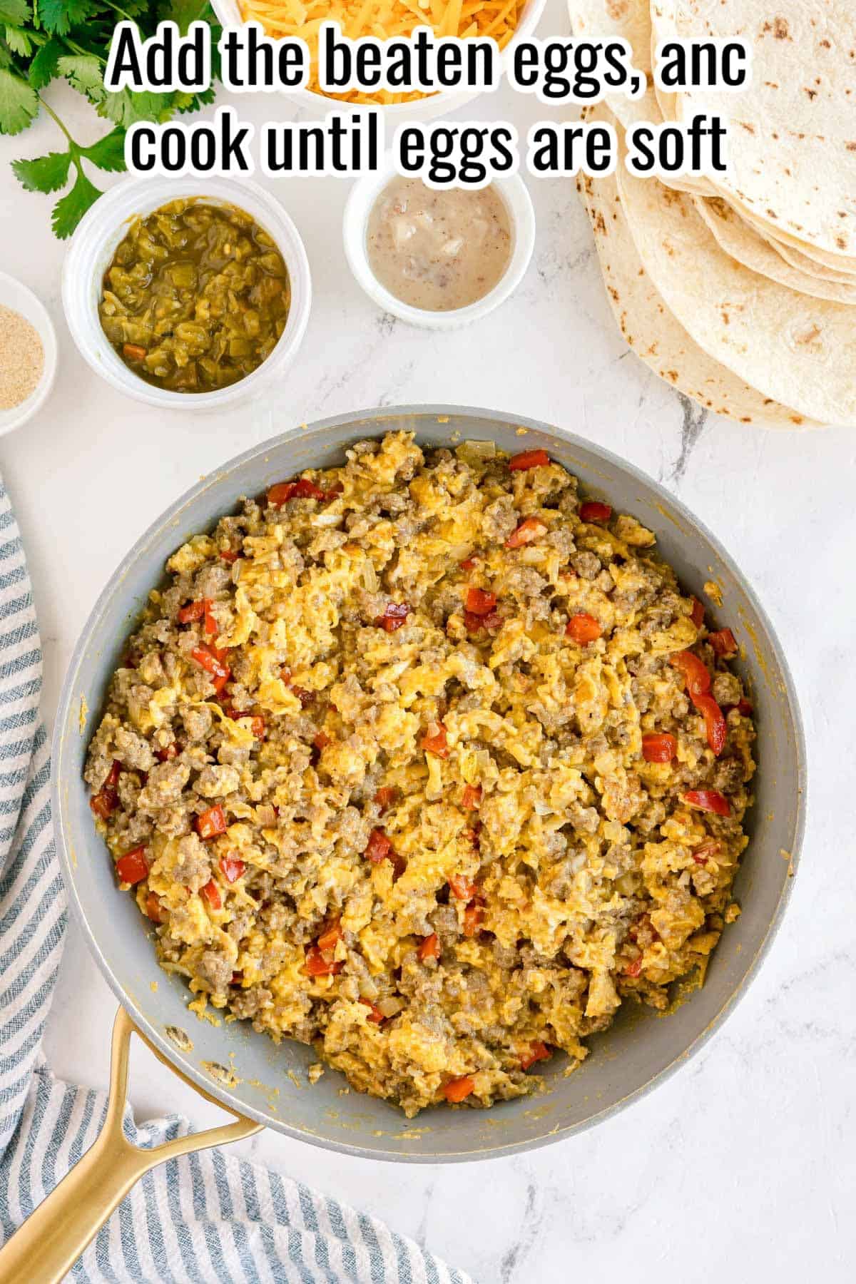 Sausage and vegetable mixture with scrambled eggs in a skillet and text overlay “Add the beaten eggs, and cook until eggs are soft.”