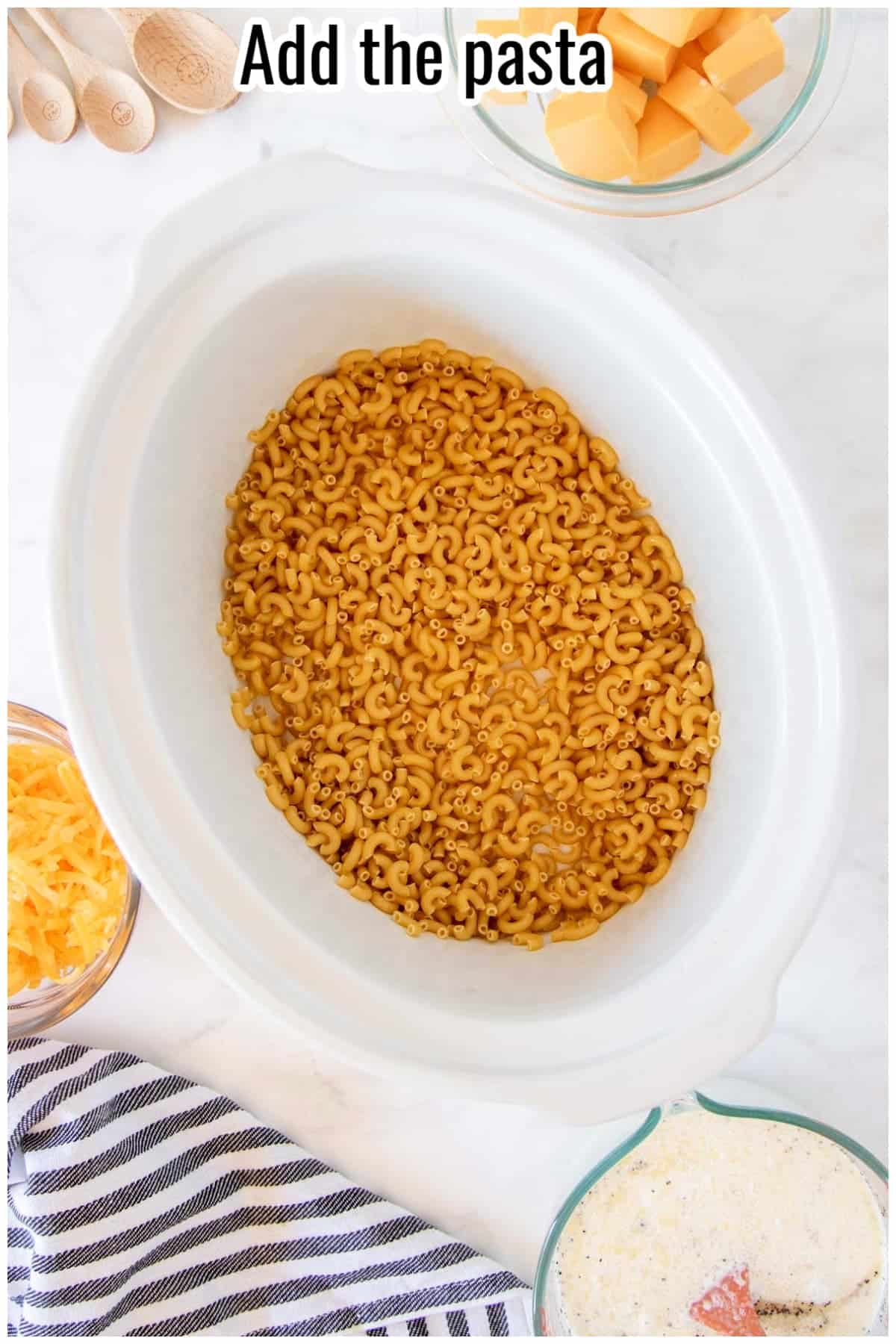 Dry macaroni pasta in a white slow cooker. Text on the image says 'Add the pasta'.