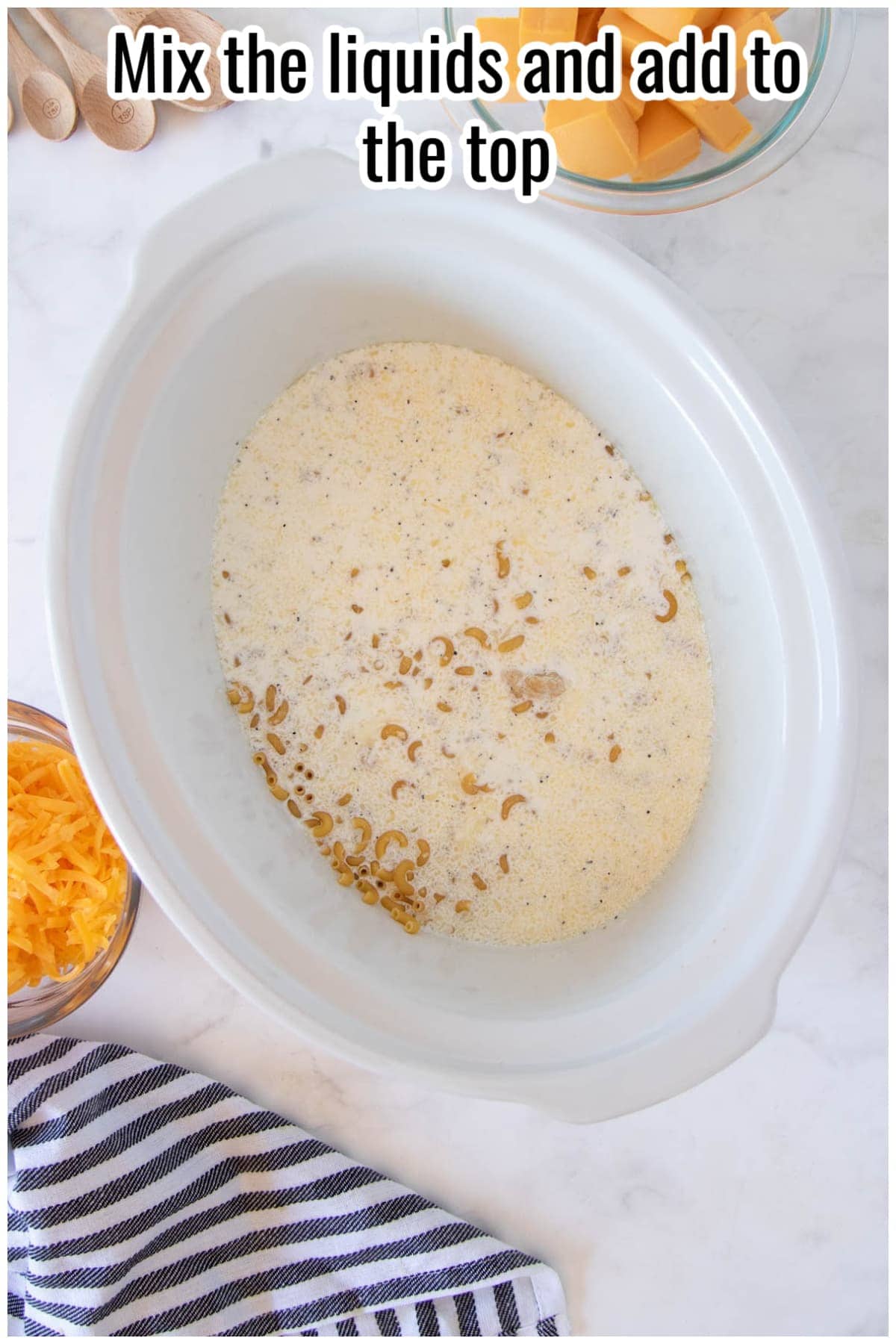 Milk mixture poured over macaroni in a white slow cooker. Text on the image says 'Mix the liquids and add to the top'.
