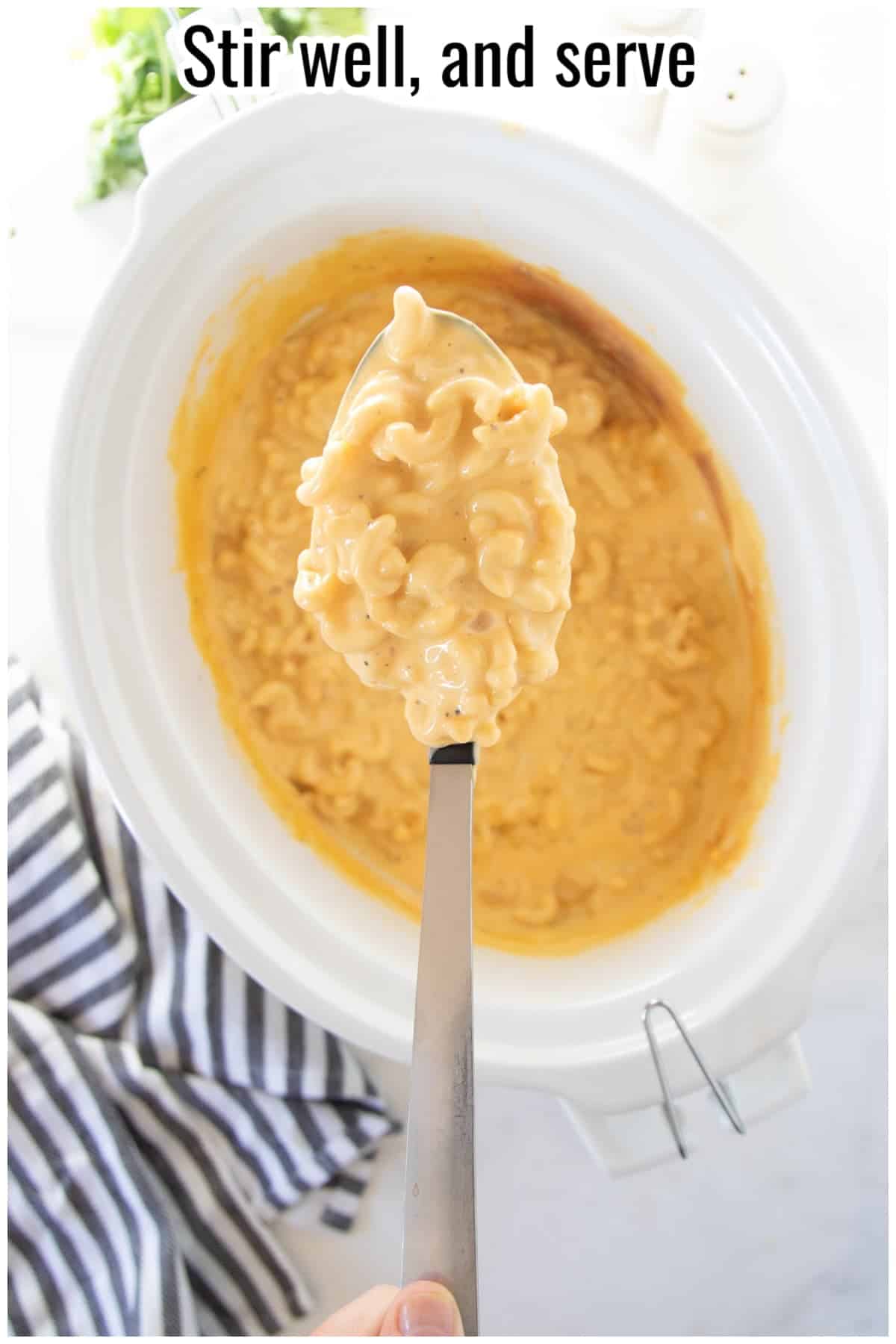 Spoon lifting creamy macaroni and cheese from a slow cooker. Text on the image says 'Stir well, and serve'.