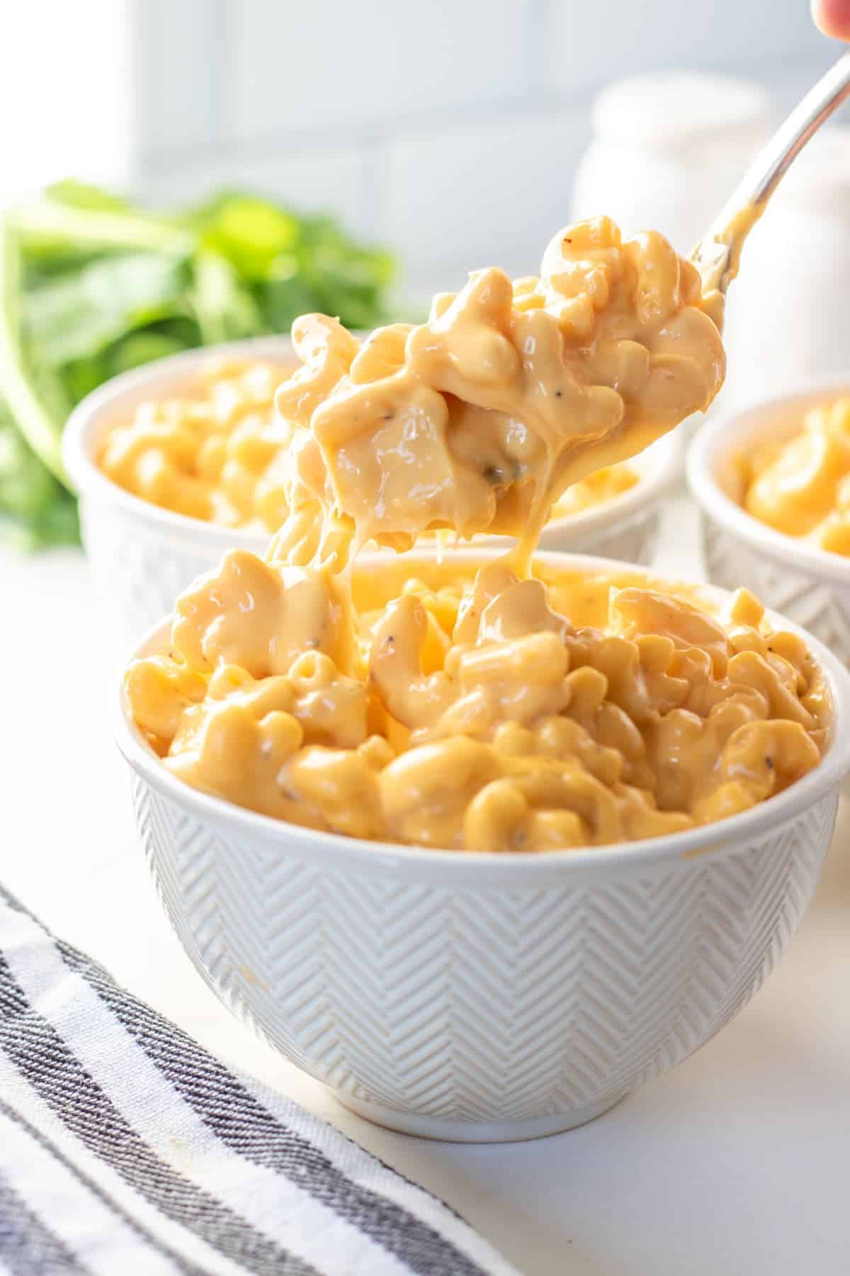 Close up of cheesy macaroni being lifted from a white bowl.