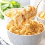 Spoon scooping creamy macaroni and cheese from a white bowl.