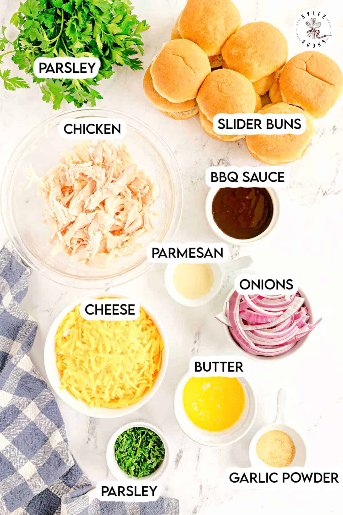 Ingredients for chicken sliders arranged on a counter, including shredded chicken, slider buns, BBQ sauce, Parmesan, shredded cheese, onions, butter, parsley, and garlic powder.