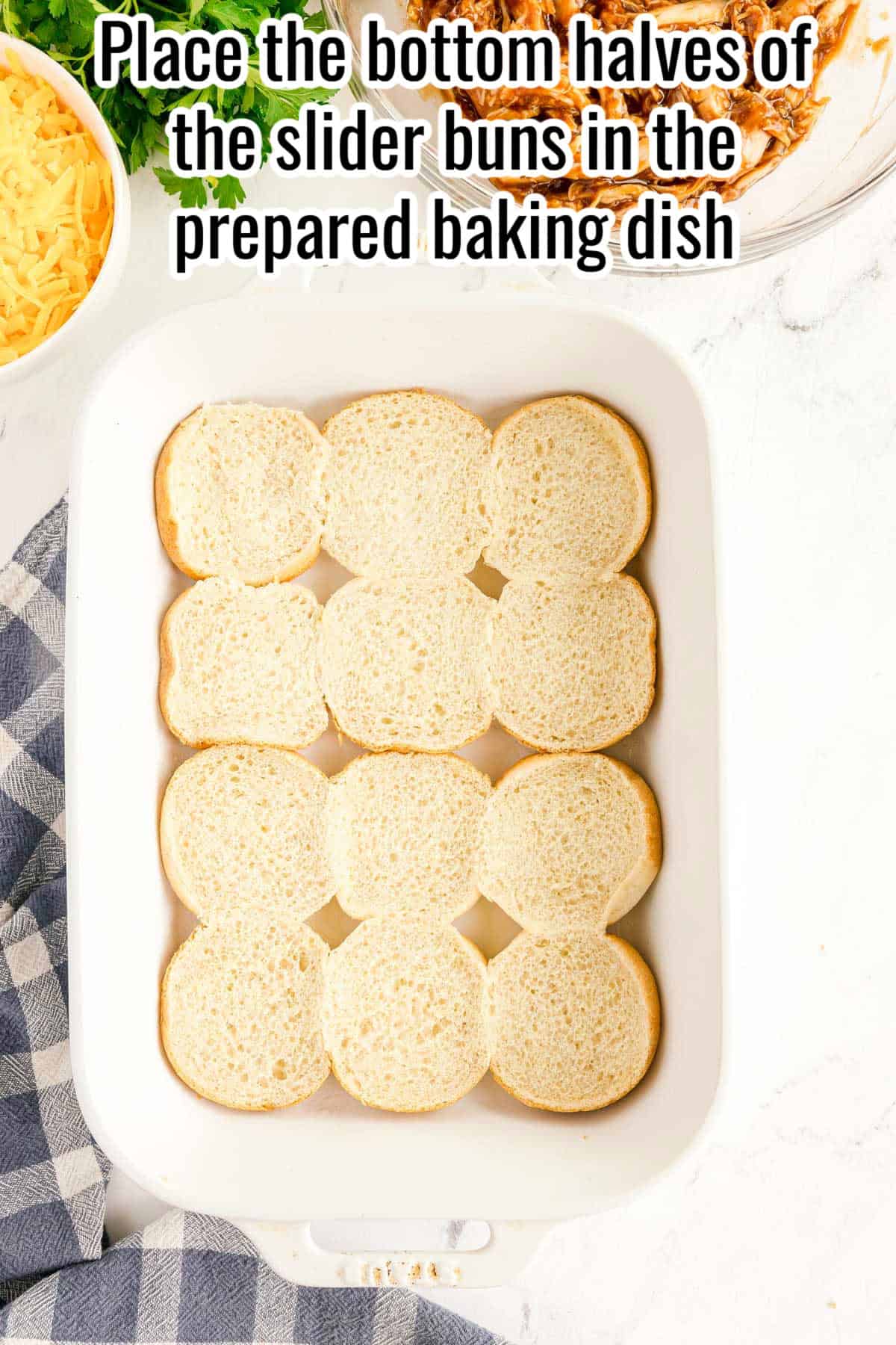A white baking dish with nine slider bun bottoms arranged in rows; text above instructs to place bun bottoms in the dish, the perfect base for assembling your bbq chicken sliders.