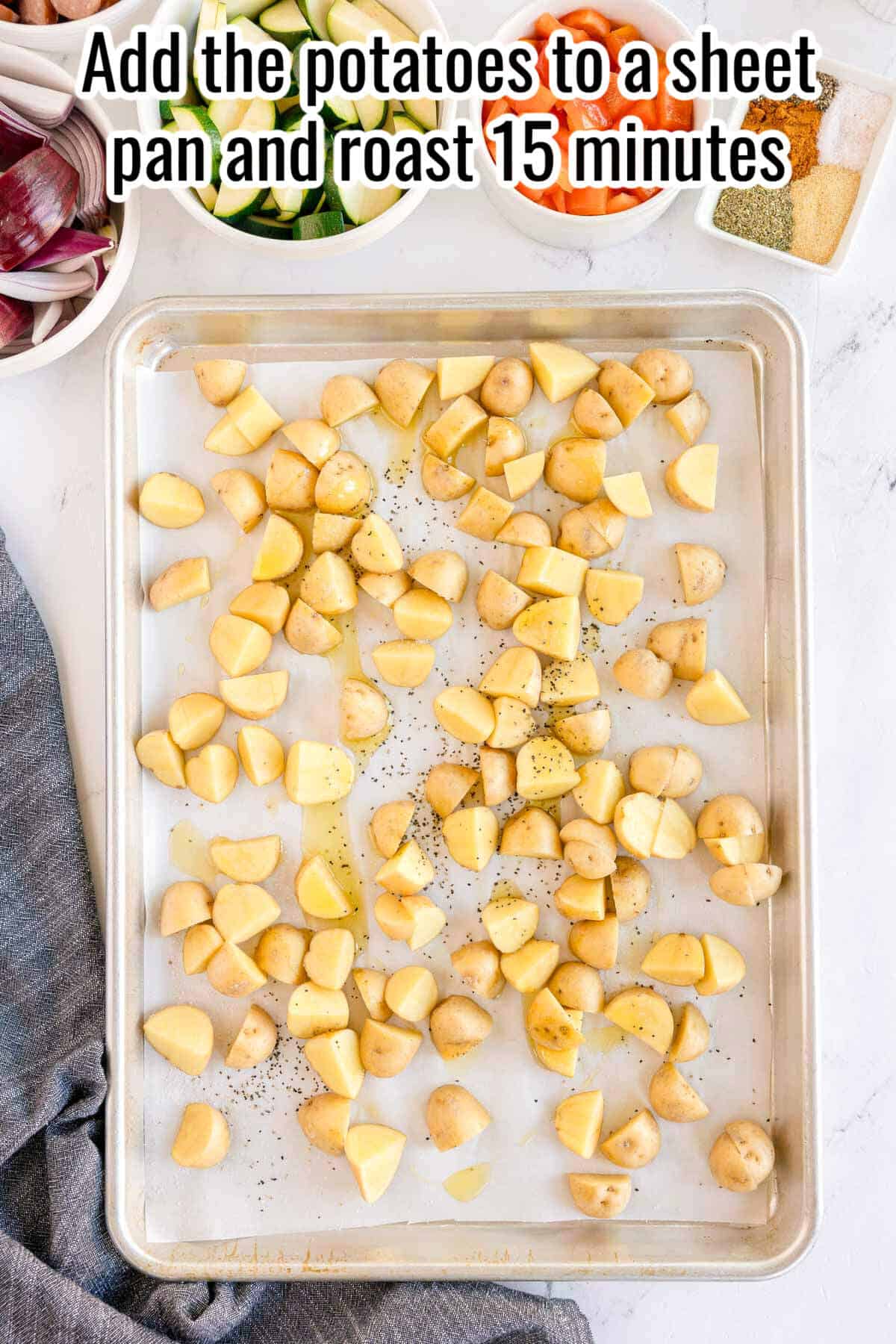 Step one of making sheet pan sausage and veggies: raw quartered potatoes spread out on a parchment-lined sheet pan, with bowls of remaining ingredients visible in the background. Text reads: Add the potatoes to a sheet pan and roast 15 minutes.