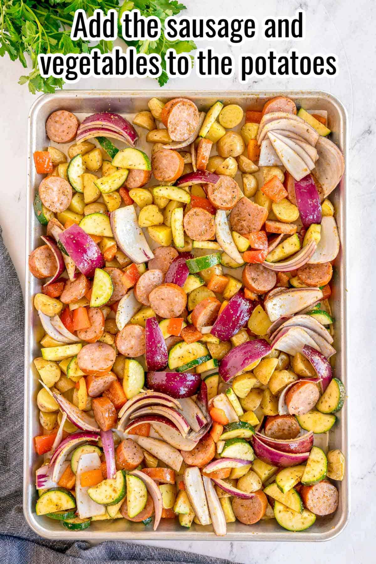 Step three of making sheet pan sausage and veggies: the seasoned sausage and vegetables added to the sheet pan alongside the partially roasted potatoes, ready to go back in the oven. Text reads: Add the sausage and vegetables to the potatoes.