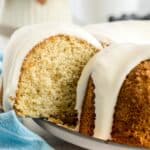A close-up of a sliced bundt cake with white icing drizzled over the top, displayed on a plate with a blue cloth nearby.