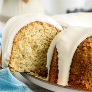 A close-up of a sliced bundt cake with white icing drizzled over the top, displayed on a plate with a blue cloth nearby.