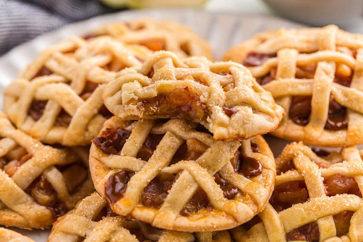 A plate of mini lattice-topped pies with fruit filling, one broken in half to show the inside.