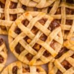 Close-up of mini lattice-topped pies with a golden crust and visible fruit filling, arranged closely together.