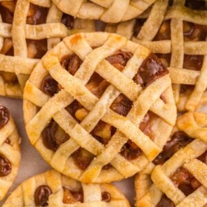 Close-up of mini lattice-topped pies with a golden crust and visible fruit filling, arranged closely together.