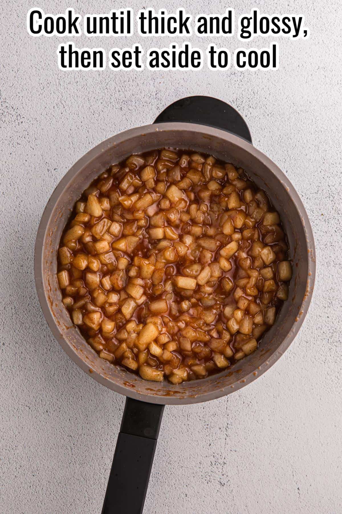 A saucepan filled with a thick, glossy, cooked apple mixture sits on a light countertop; text above instructs to let it cool.