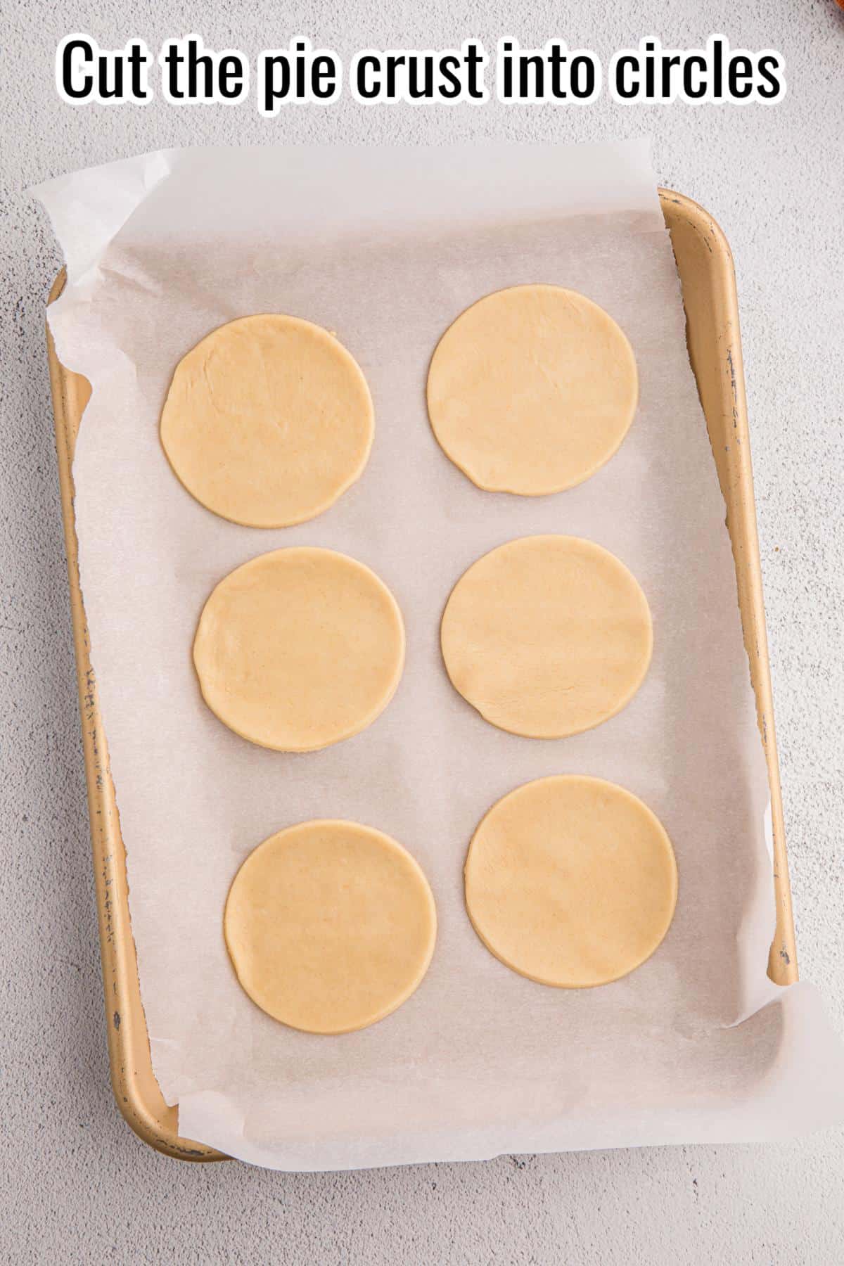 A baking sheet lined with parchment paper holds six evenly spaced, circular pie crust cutouts. Text at the top reads, "Cut the pie crust into circles.