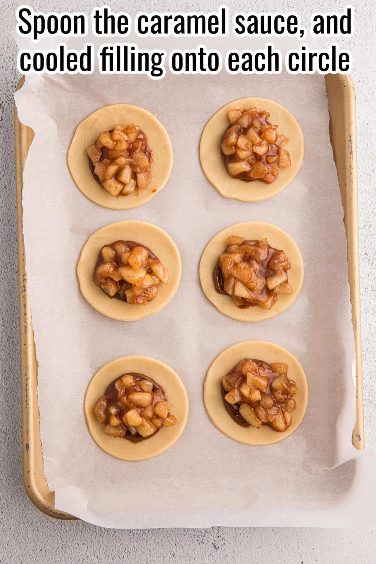 Six round dough circles on a parchment-lined baking sheet, each topped with caramel apple filling. Text at top instructs to spoon caramel sauce and filling onto each circle.