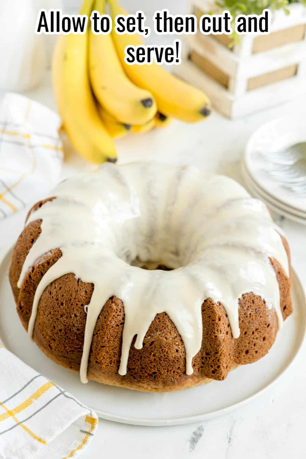 A bundt cake with white icing on a white plate, with bananas and stacked plates in the background; text reads, "Allow to set, then cut and serve!.