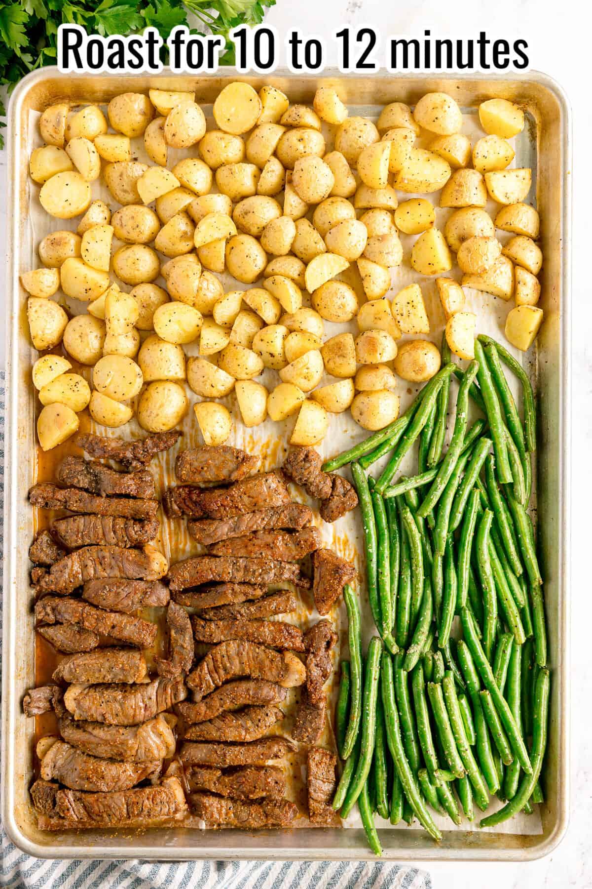 Sheet pan with seasoned potato pieces, green beans, and strips of beef arranged in rows, ready to roast for 10 to 12 minutes.