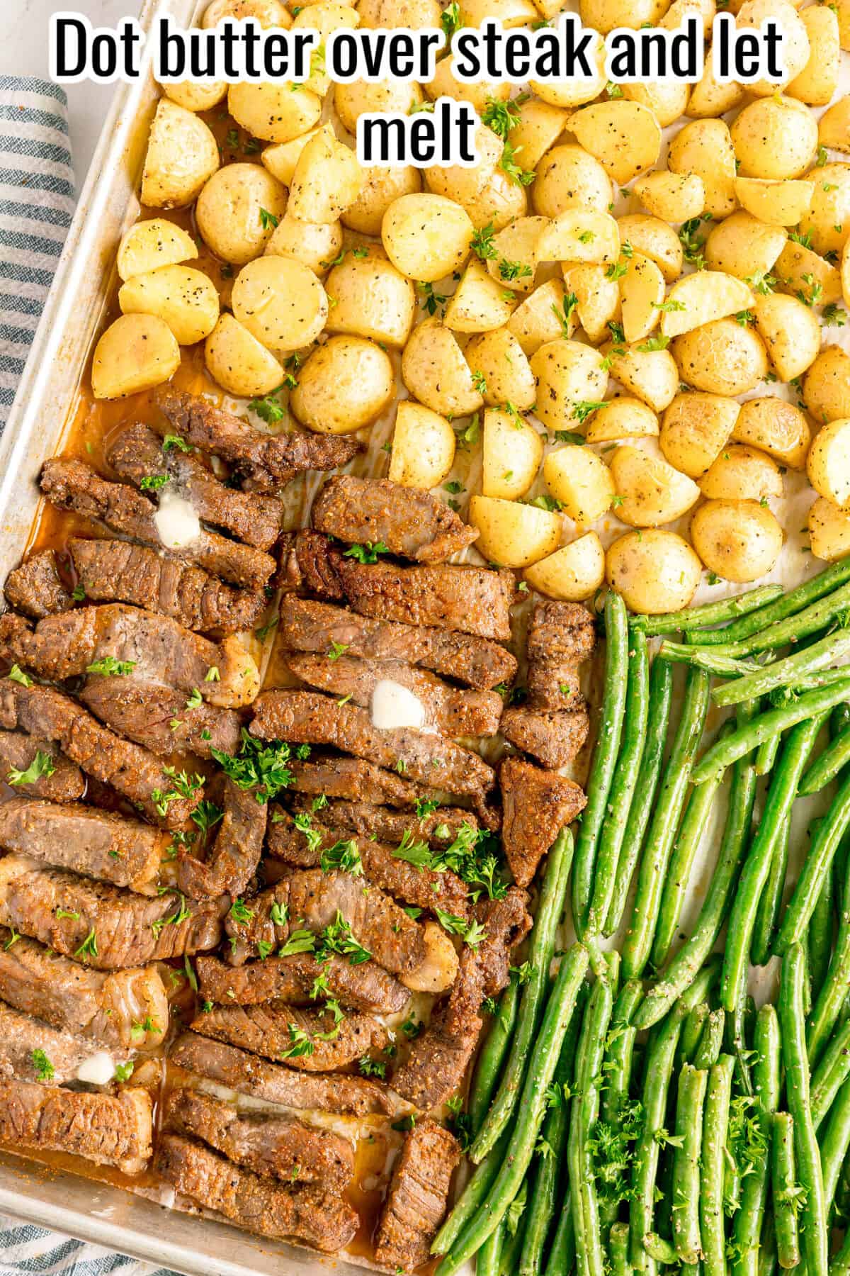 Sheet pan with sliced steak topped with melting butter, roasted baby potatoes, and cooked green beans, garnished with chopped parsley.