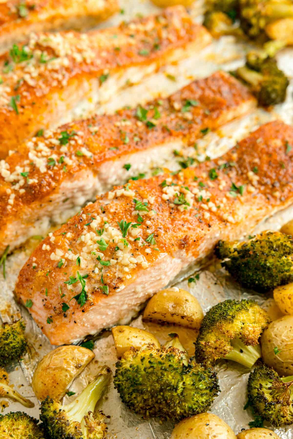 Baked salmon fillets topped with herbs and garlic, served with roasted broccoli and potatoes on a sheet pan.