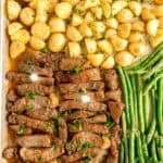 Sheet pan with roasted baby potatoes, sliced steak topped with herbs and butter, and green beans arranged in separate sections.