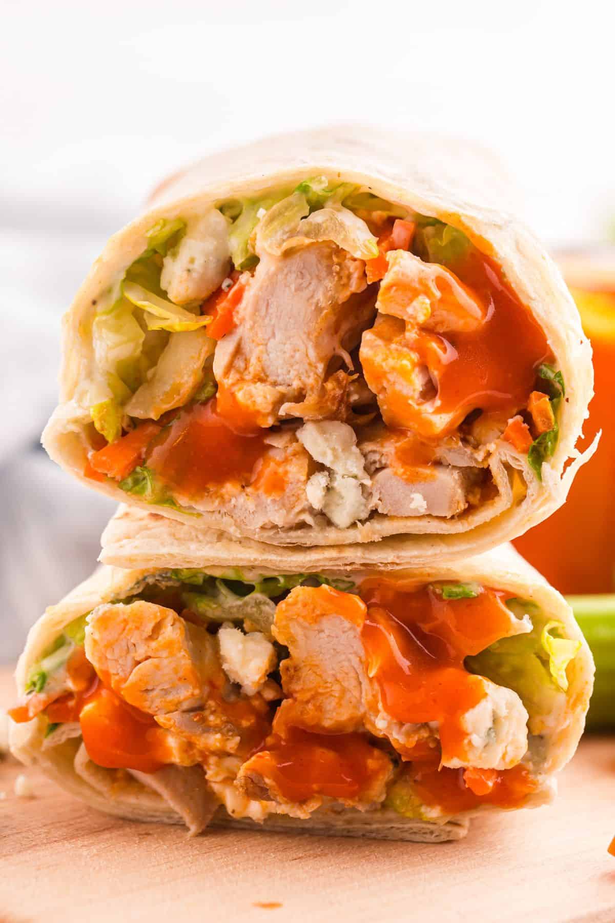 A close-up of a wrap cut in half, filled with pieces of chicken, lettuce, crumbled cheese, and a generous amount of red sauce.