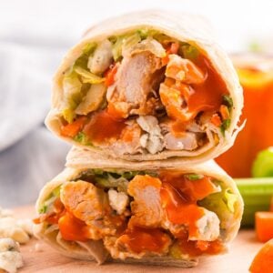 A close-up of a halved buffalo chicken wrap showing pieces of chicken, lettuce, carrots, blue cheese, and buffalo sauce inside a tortilla.