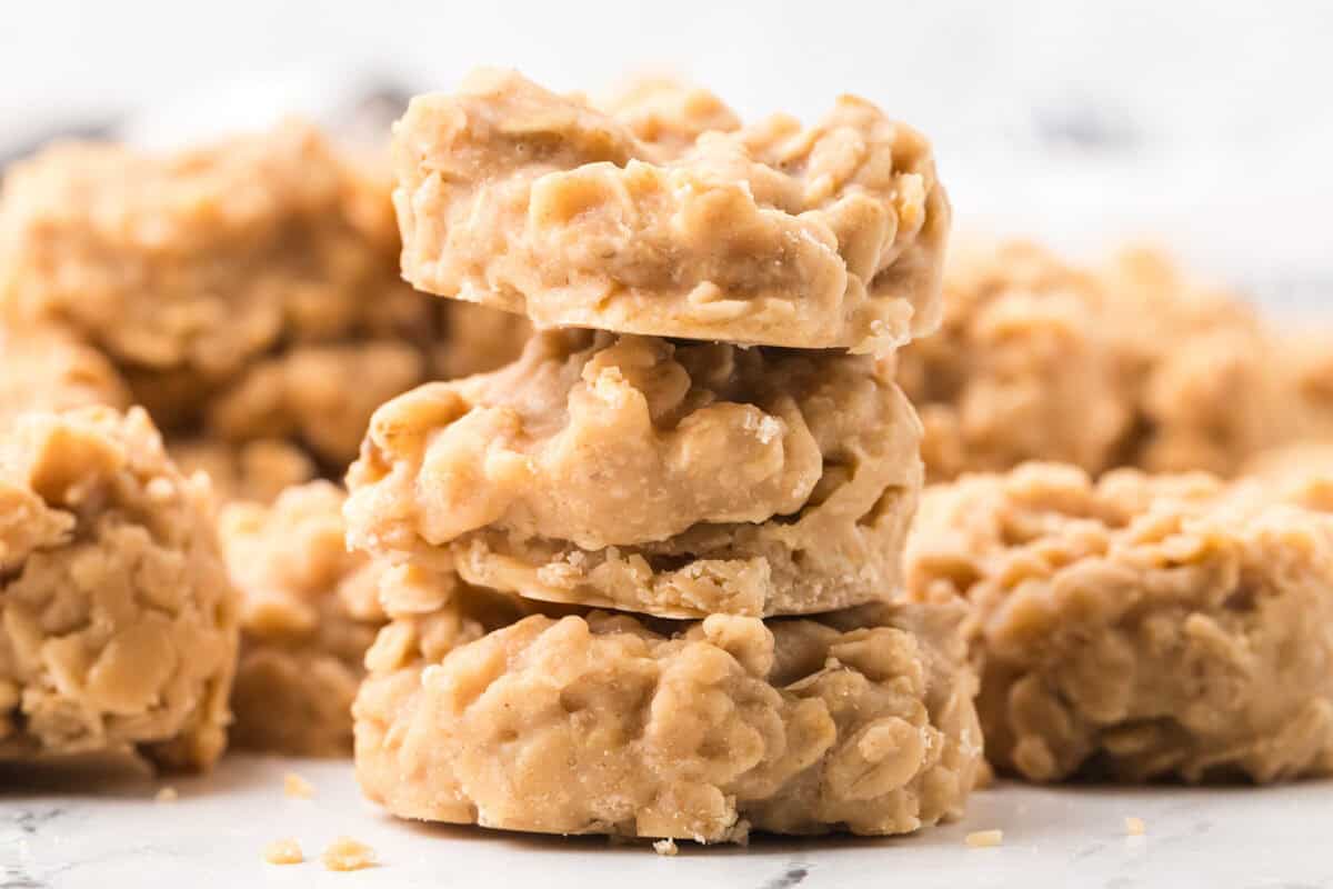 A close-up of a stack of three no-bake peanut butter oatmeal cookies with more cookies blurred in the background.
