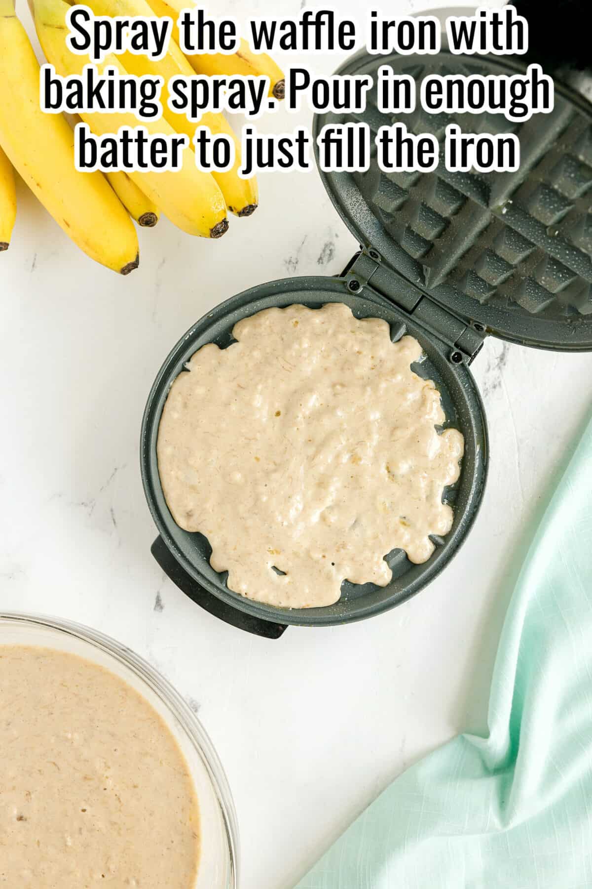 Open waffle iron filled with batter, surrounded by bananas, a bowl of batter, and a light blue cloth. Text instructions appear at the top.