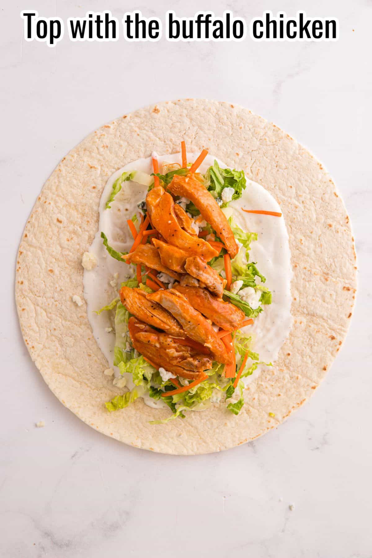 A tortilla topped with shredded lettuce, carrot sticks, ranch sauce, and buffalo chicken strips, with text reading "Top with the buffalo chicken" at the top.