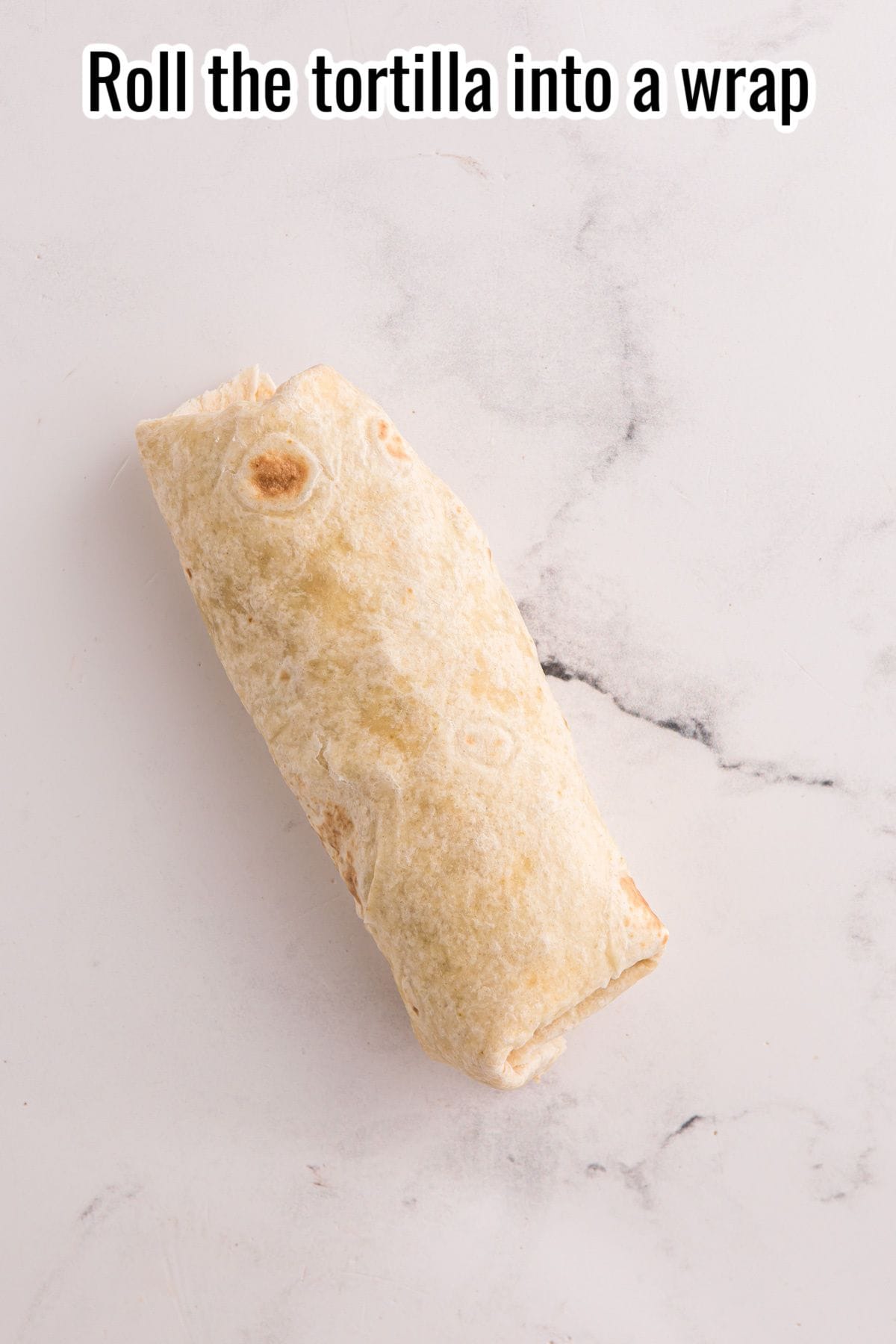 A Buffalo Chicken Wrap placed on a white marble surface with the text "Roll the tortilla into a wrap" above it.