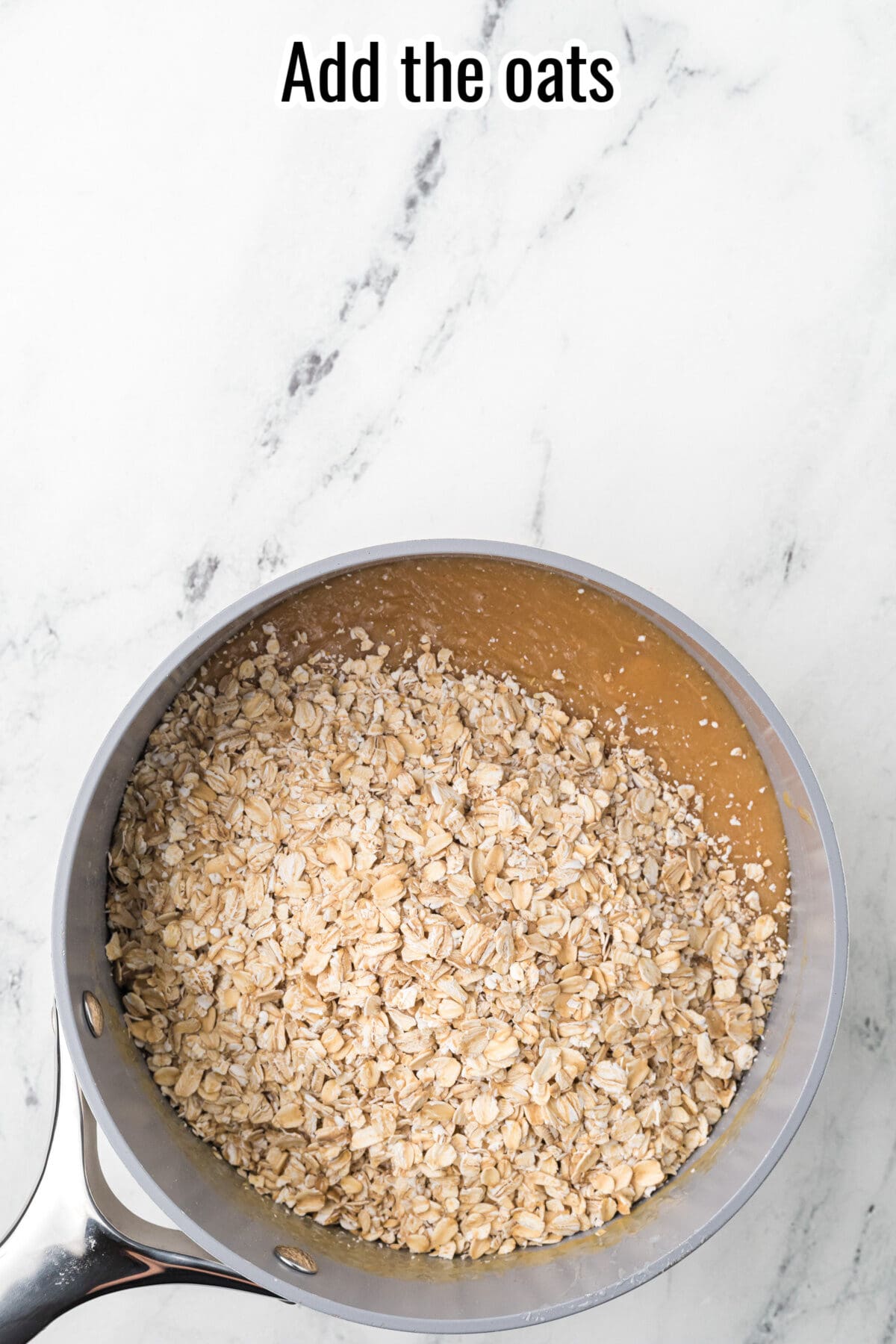 A saucepan filled with dry oats sits on a marble countertop. Text at the top reads, "Add the oats.
