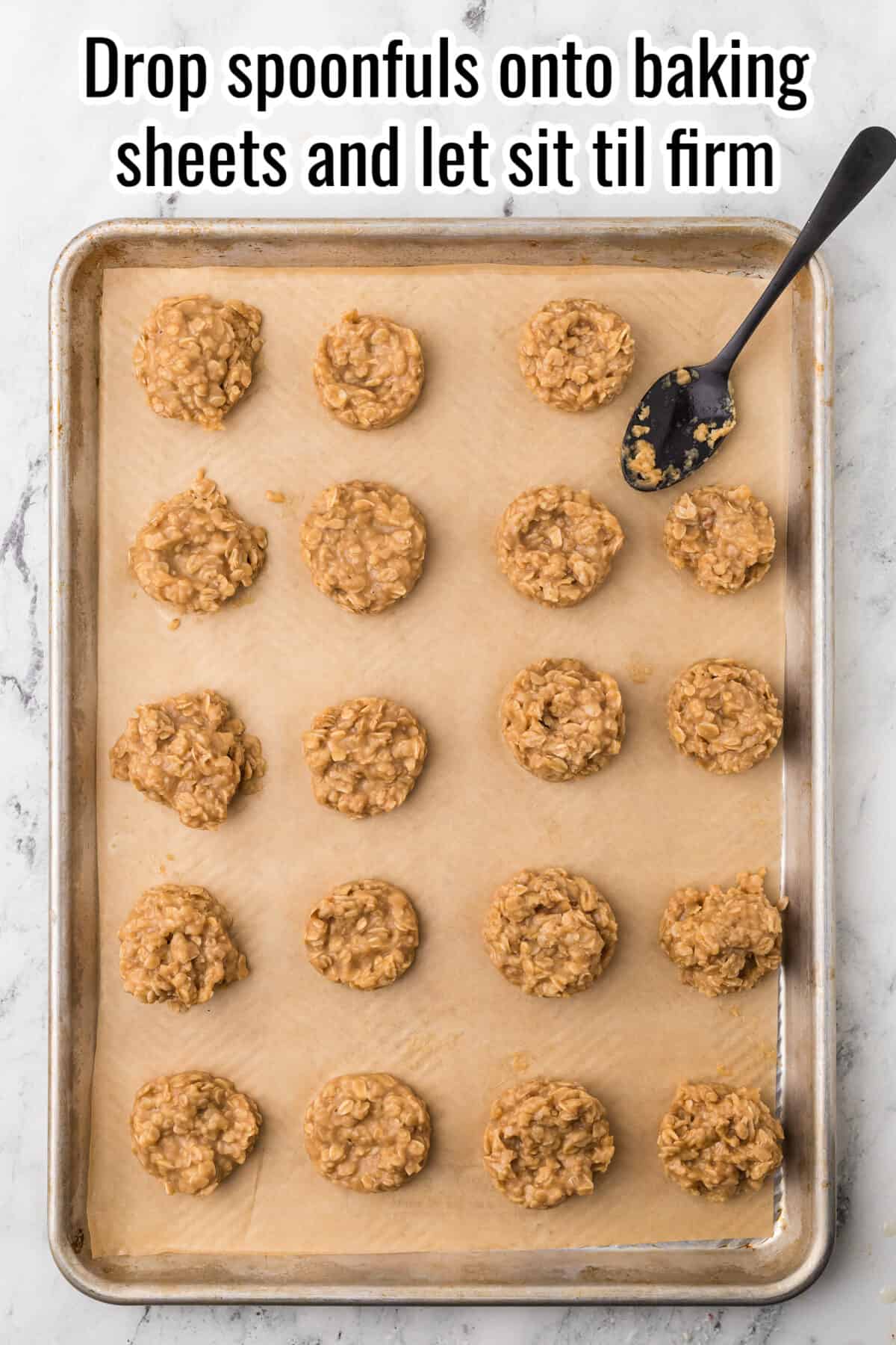 Twenty round cookie dough portions are arranged on a parchment-lined baking sheet with a spoon, ready to set. Instructions read: "Drop spoonfuls onto baking sheets and let sit til firm.