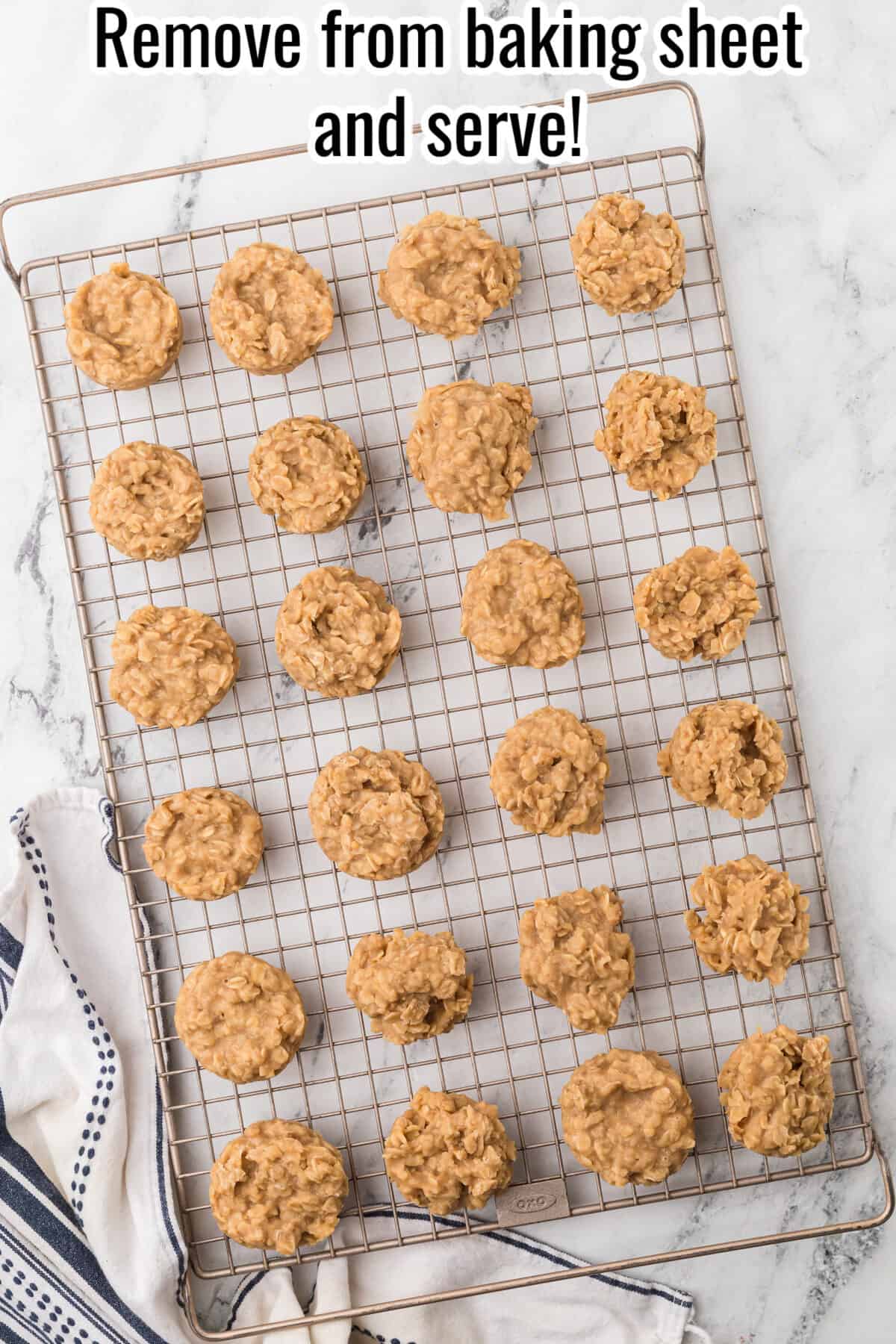A top-down view of freshly baked no-bake oatmeal cookies cooling on a wire rack over a white marble surface, next to a blue-and-white striped towel. Text at the top reads, "Remove from baking sheet and serve!.