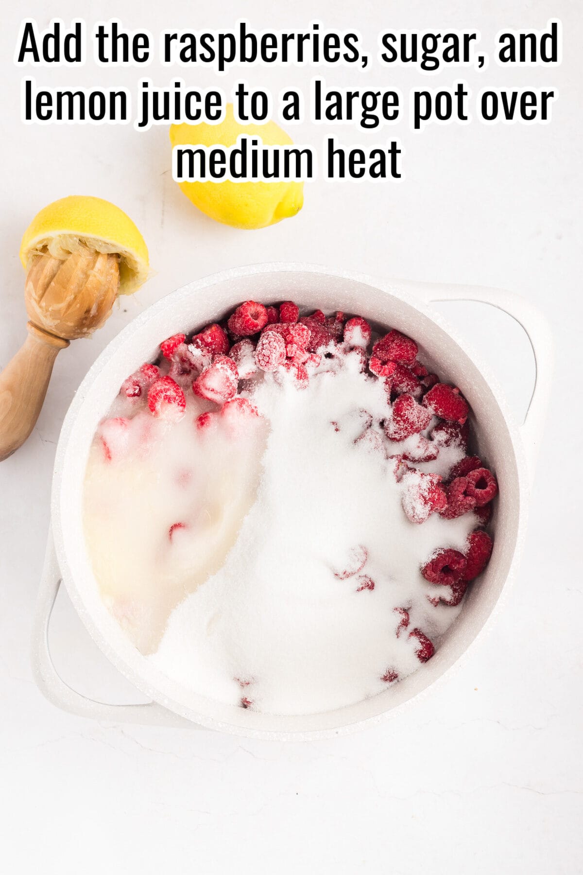 Pot filled with raspberries, sugar, and lemon juice sits on a white surface beside a juiced lemon and wooden reamer. Text instructions appear at the top of the image.