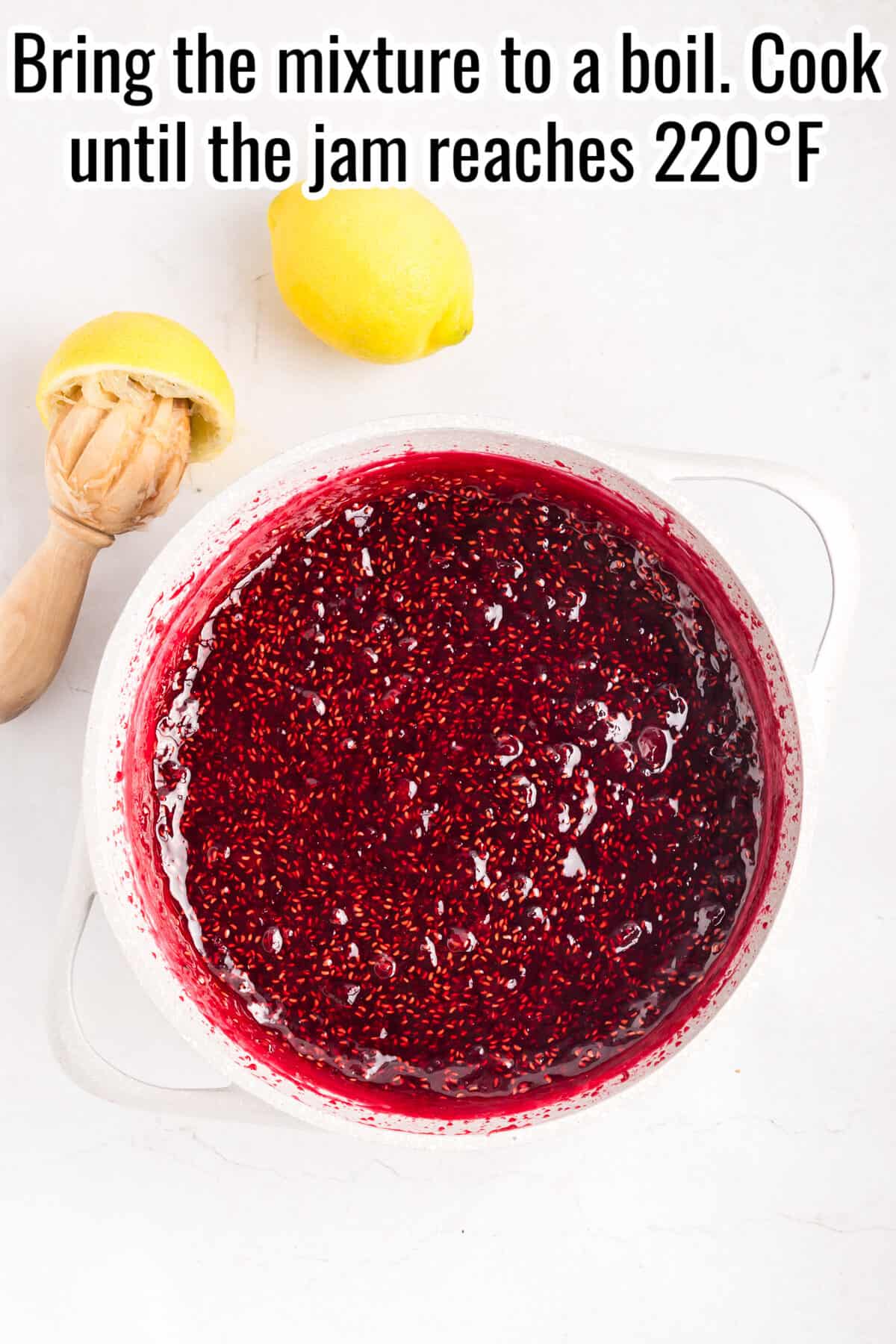 A pot of raspberry jam cooking on a white surface with a lemon, lemon reamer, and text instructions above.