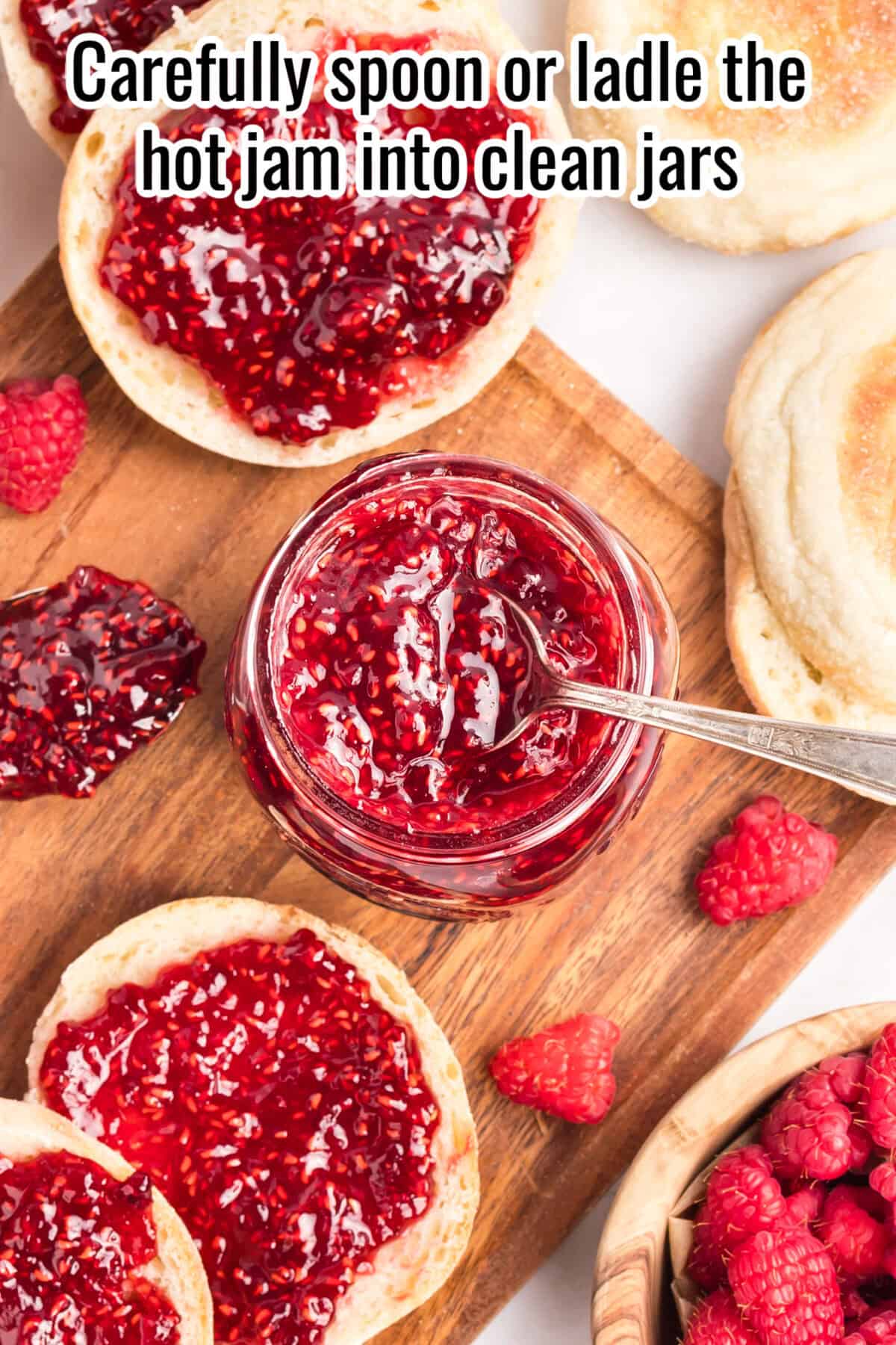 A jar of raspberry jam with a spoon sits on a wooden board surrounded by muffins, fresh raspberries, and spilled jam. Text reads: "Carefully spoon or ladle the hot jam into clean jars.