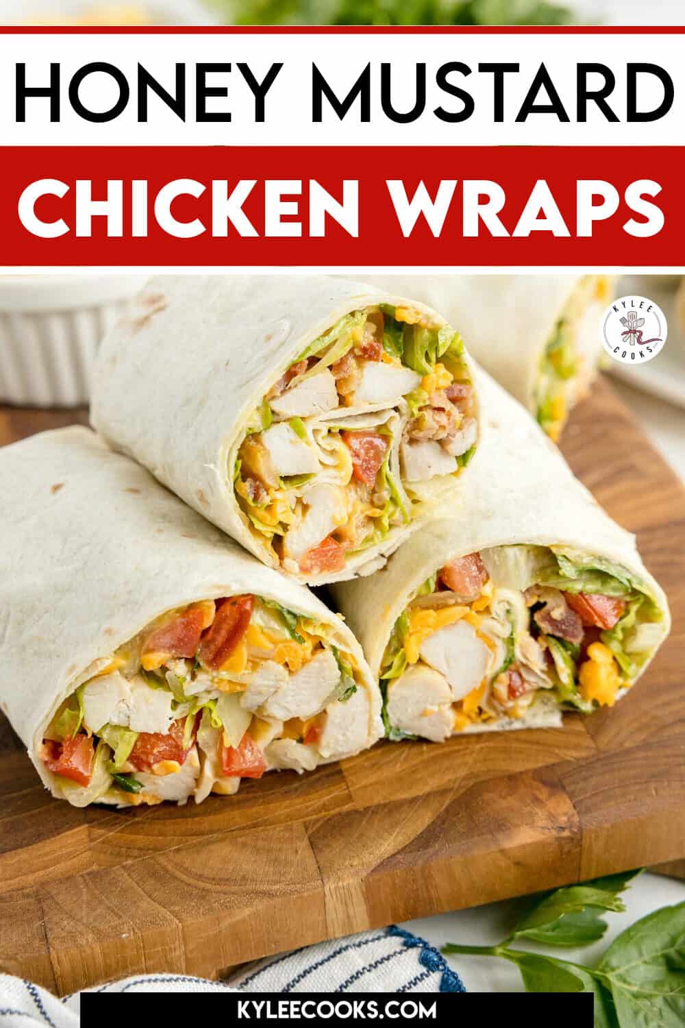 Three honey mustard chicken wraps filled with lettuce, tomato, and cheese are stacked on a wooden cutting board.