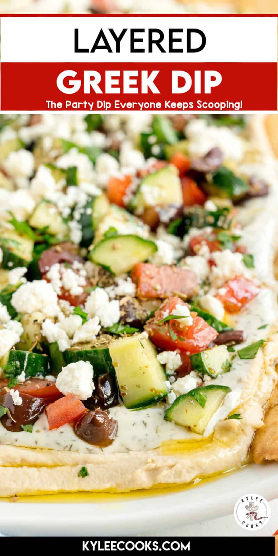 Close-up of a layered Greek dip with chopped cucumbers, tomatoes, olives, feta cheese, herbs, and dip on a platter.