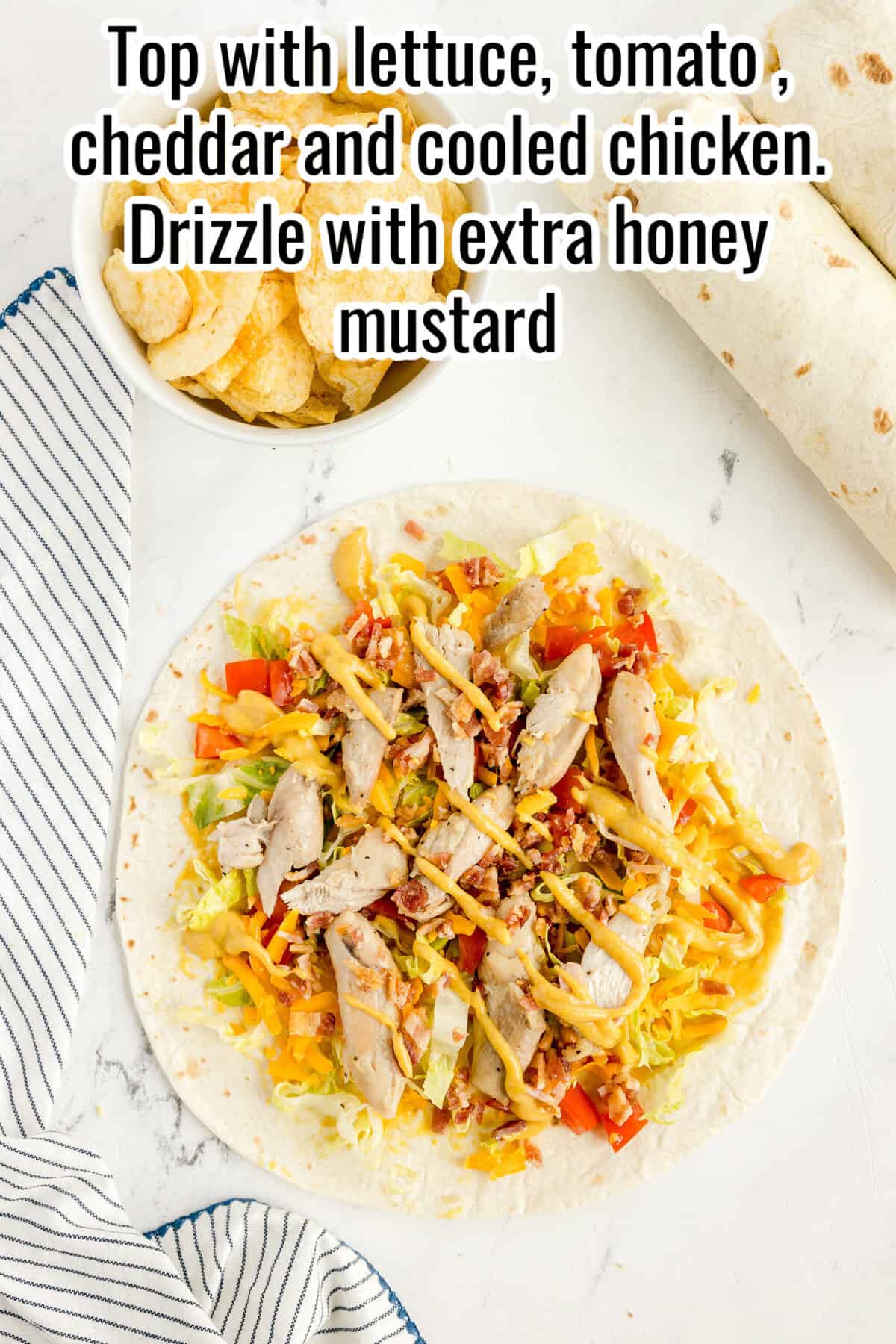 A tortilla topped with shredded lettuce, diced tomato, cheddar cheese, and sliced chicken, with honey mustard drizzled on top. A bowl of chips and tortillas are nearby.