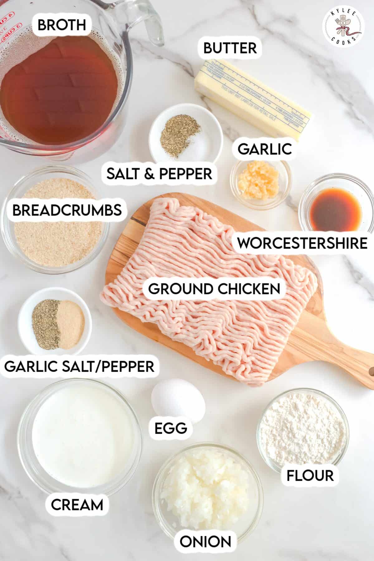 Ingredients for a chicken recipe on a white surface: broth, butter, garlic, Worcestershire, spices, breadcrumbs, ground chicken, cream, onion, flour, and an egg.