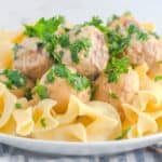 A plate of egg noodles topped with several meatballs and garnished with chopped fresh parsley.