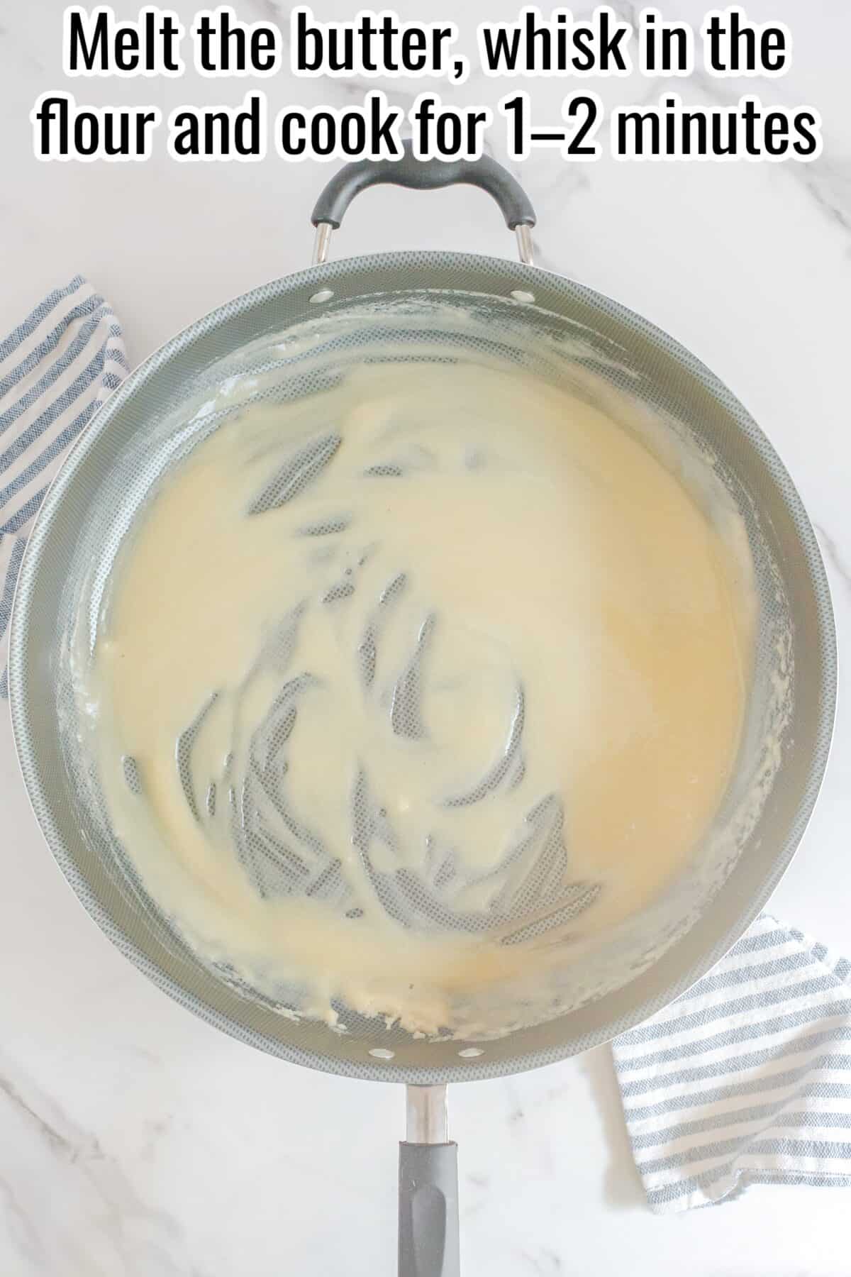 A pan with melted butter and flour being whisked together, forming a roux; a striped towel is beside the pan.
