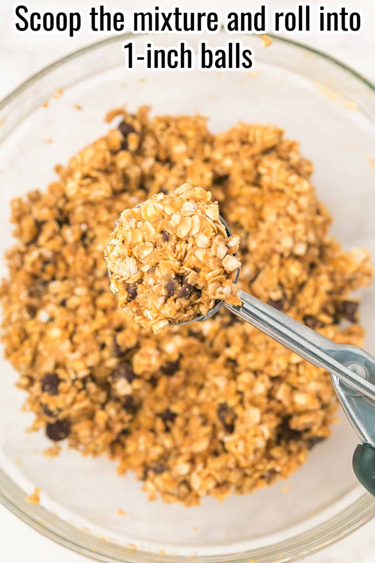 An ice cream scoop lifts a ball of oat and chocolate chip mixture over a glass bowl filled with the same mixture.