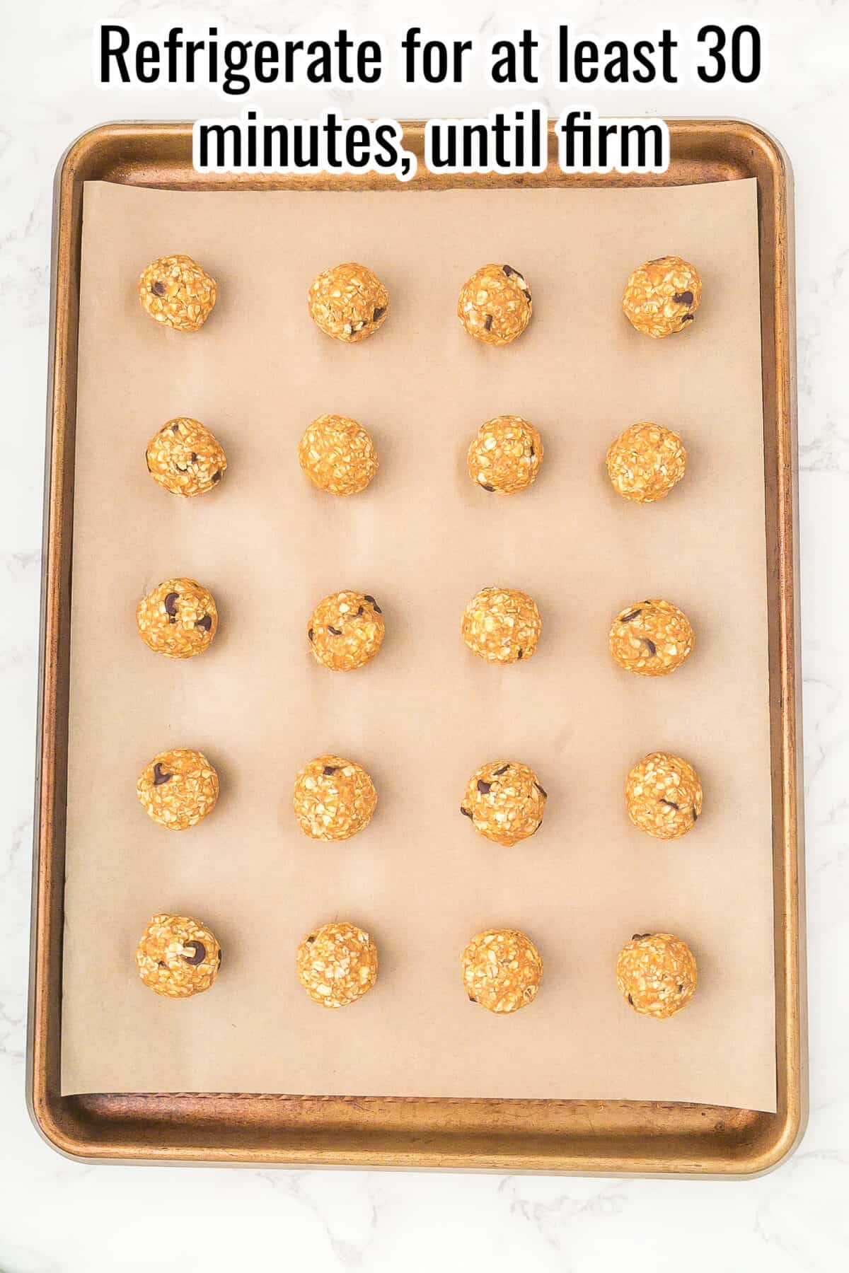 A baking sheet lined with parchment paper holds 20 evenly spaced, round oat and chocolate chip cookie dough balls. Text at the top instructs to refrigerate for at least 30 minutes, until firm.