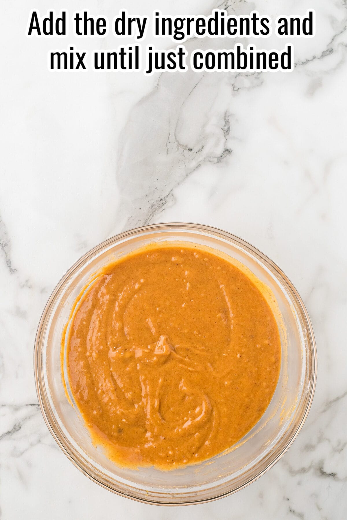 A glass bowl containing a smooth, orange batter, with the text overlay: “Add the dry ingredients and mix until just combined.”
