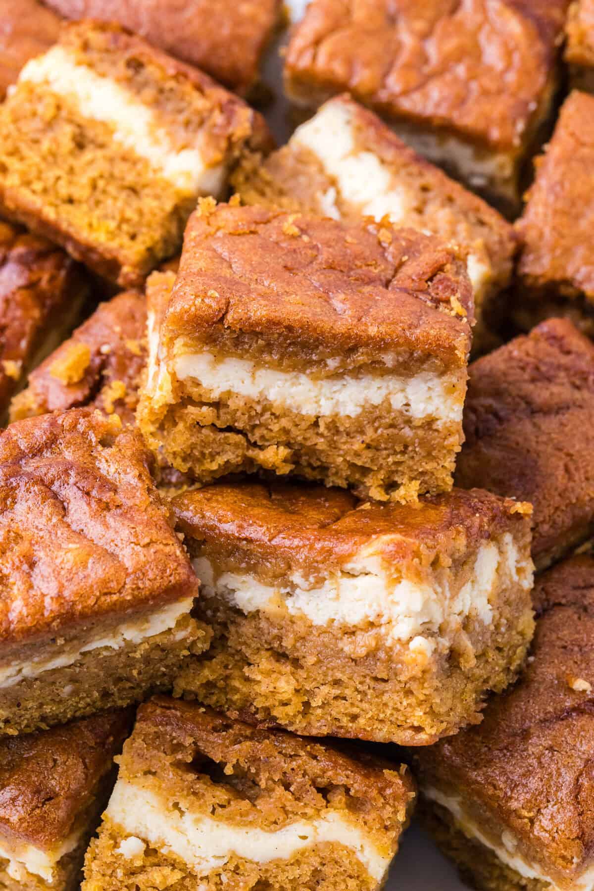 A stack of pumpkin cheesecake bars with a creamy white filling between two layers of spiced cake.
